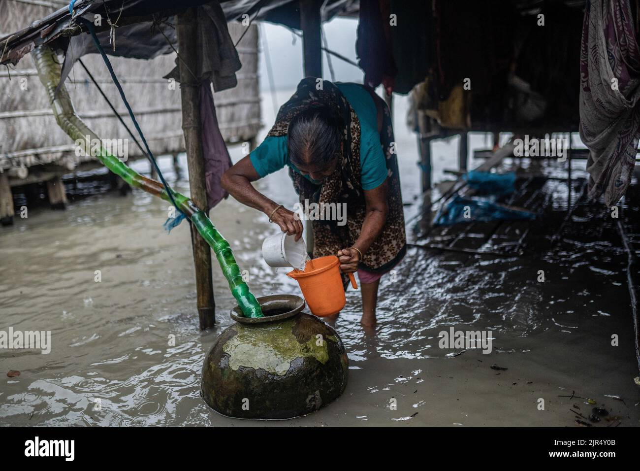 August 19, 2022, Kalabogi, Bangladesh: A woman tries to fill up her mag from the rainwater which comes from the pet bottle-made pipe at Kalabogi village in Khulna. Not too long ago Kalabogi, a coastal village in Bangladesh, was full of cultivable land until the rising sea levels began to swallow the area all the way up to the Bay of Bengal. Frequent cyclones and floods hit the village since the late 1990s. In 2009, a major cyclone named Aila destroyed the country's 1,400 kilometres of embankments, 8,800 kilometres of roads, and about 3, 50,000 acres of farmland. Several hundred people were rep Stock Photo