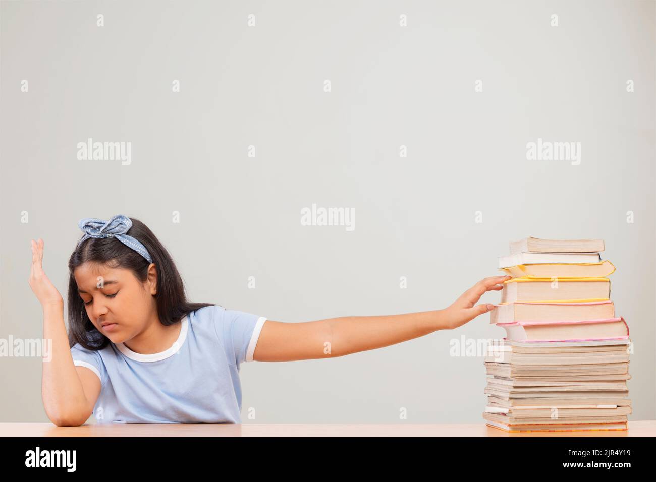 Girl expressing reluctance while sitting beside a stack of books Stock Photo