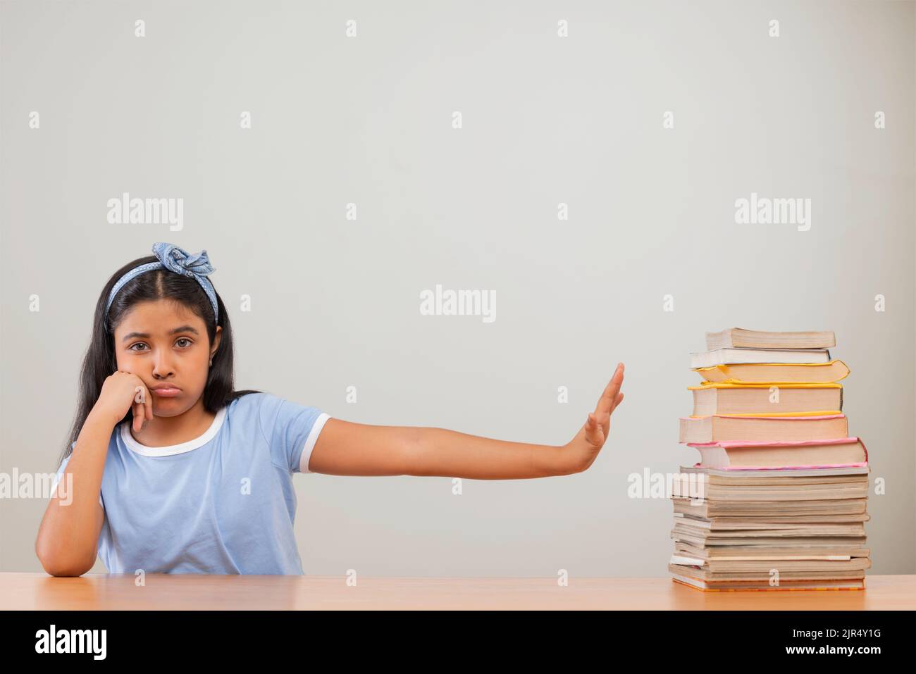 Girl expressing reluctance while sitting beside a stack of books Stock Photo