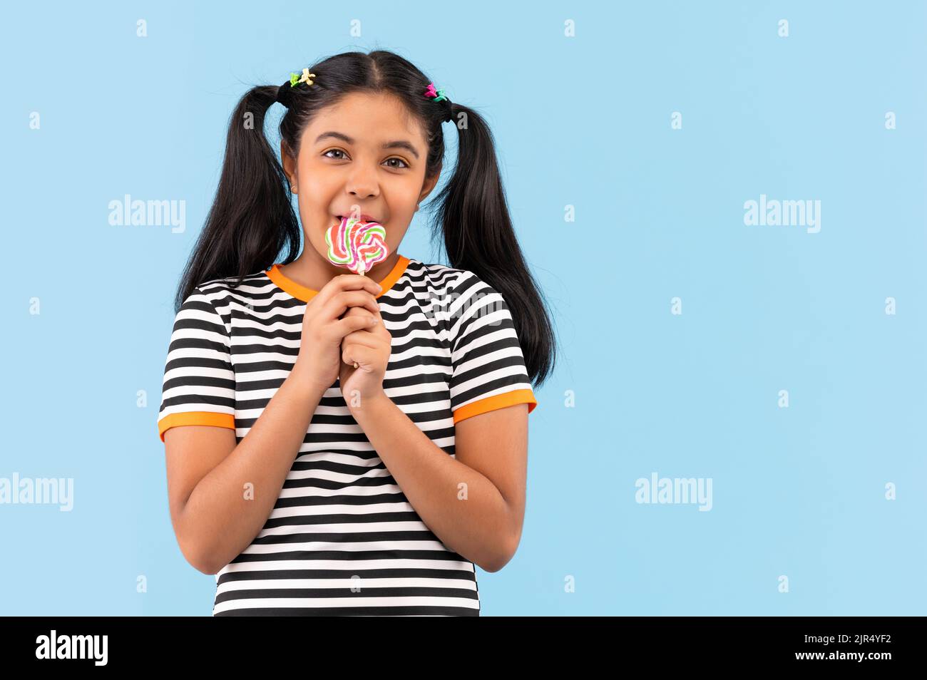 Portrait of little girl licking lollipop against plain background Stock Photo