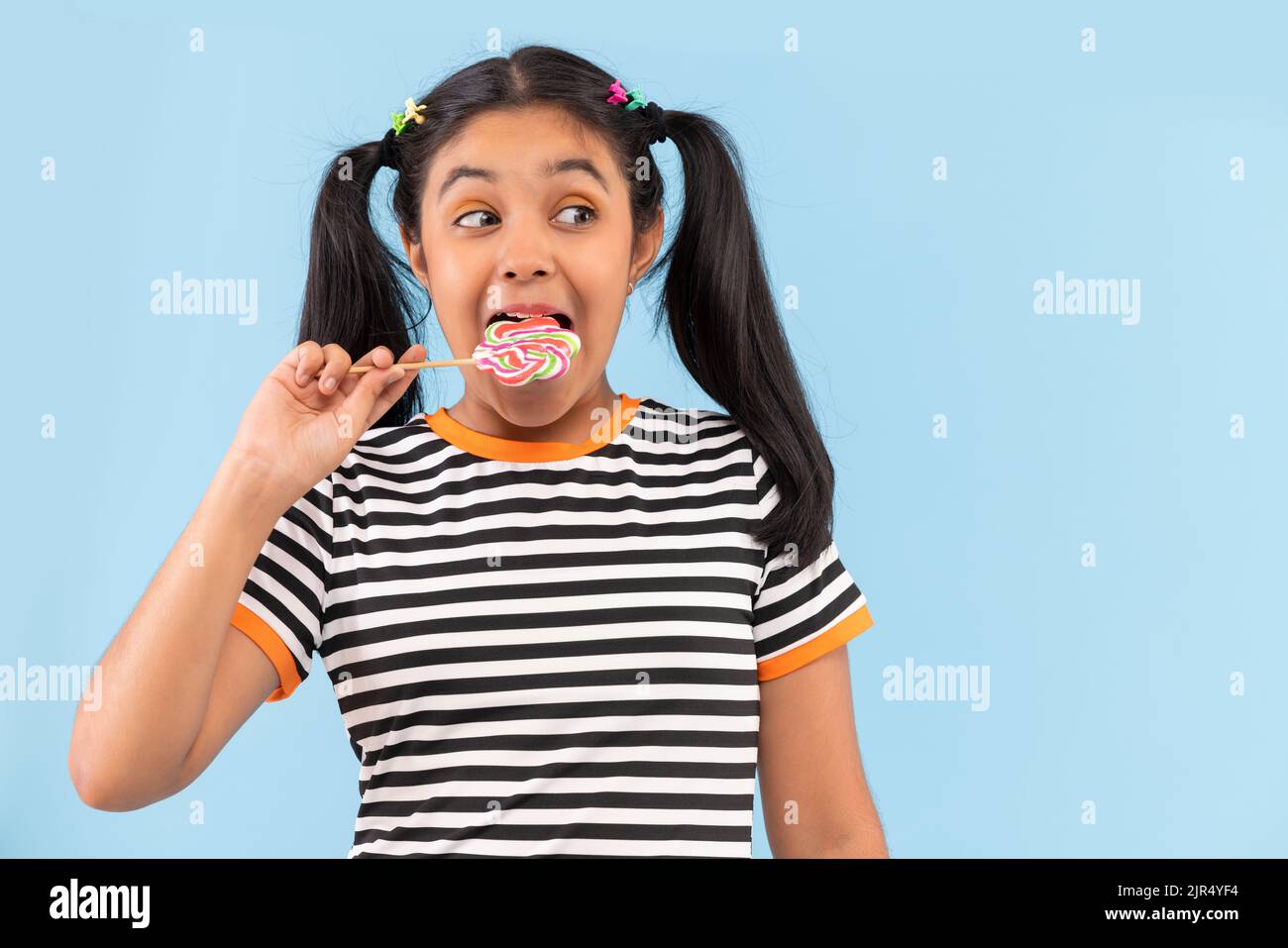 Close-up of little girl licking lollipop against plain background Stock Photo