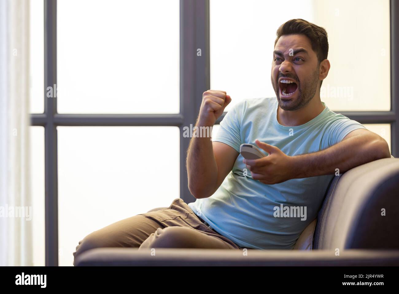 Excited man cheering while watching TV at home Stock Photo
