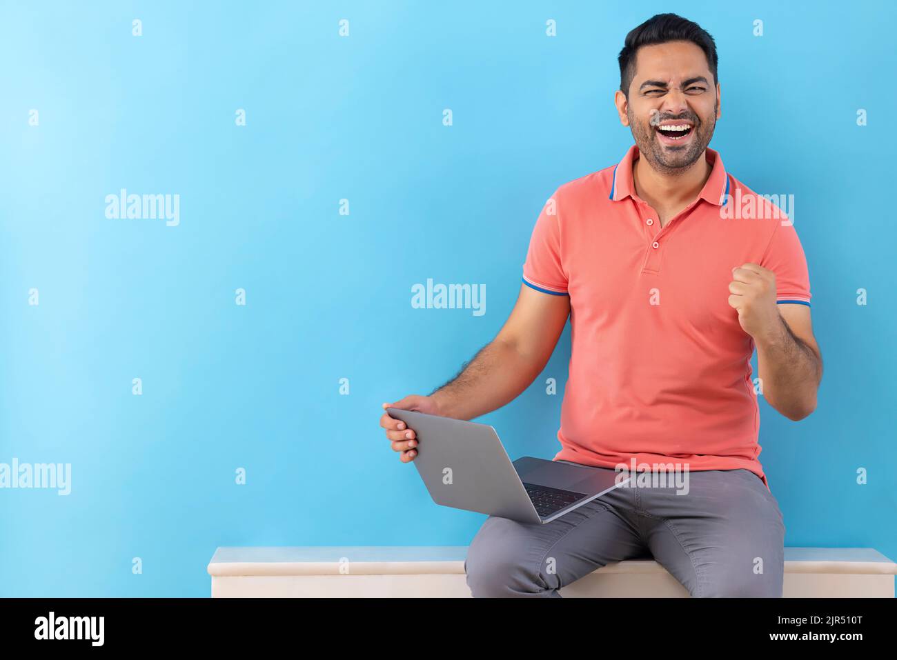 Happy young man cheering by raising fist while using laptop Stock Photo
