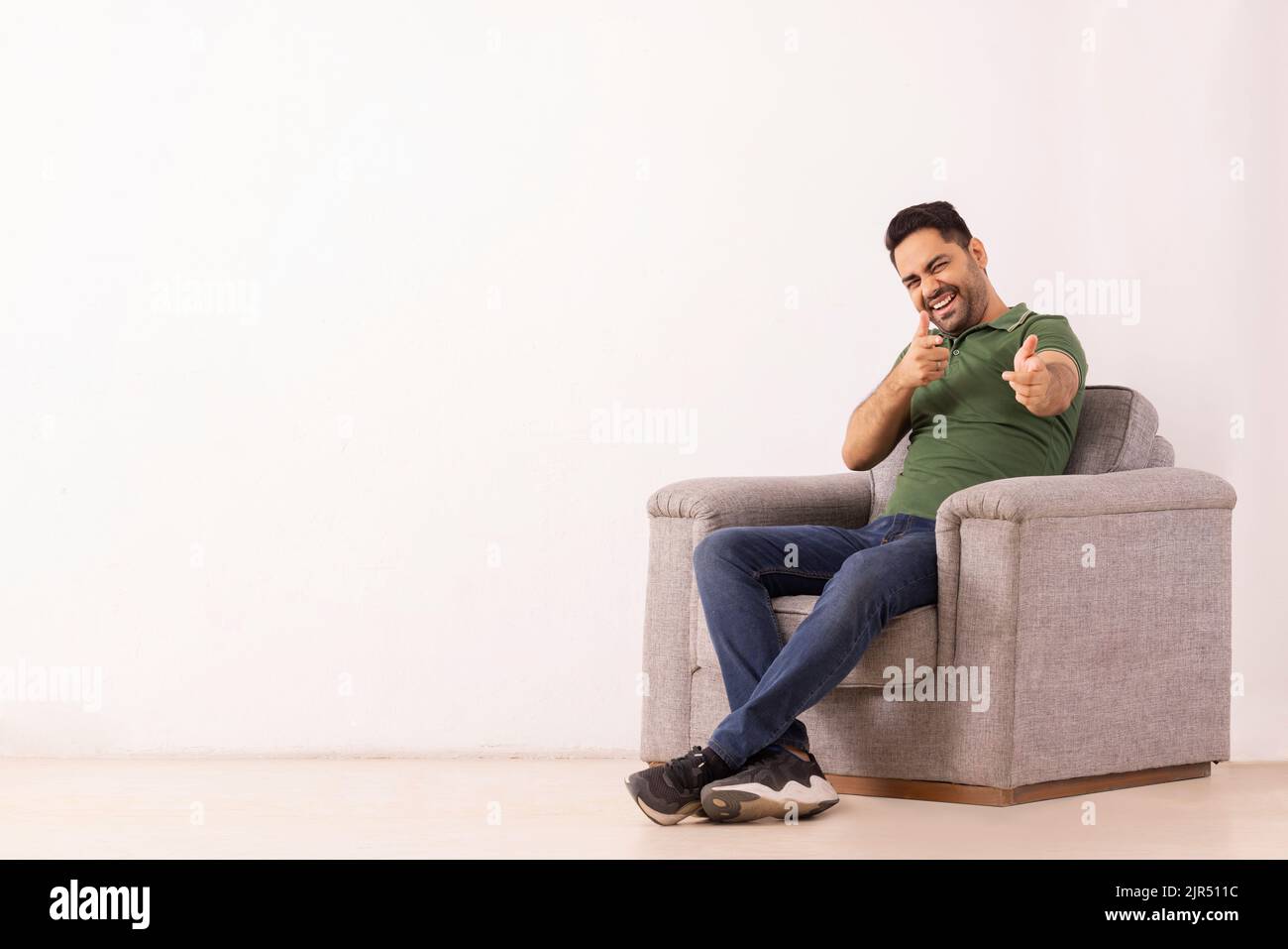 Portrait of a smiling young man looking and pointing at camera while sitting on sofa Stock Photo