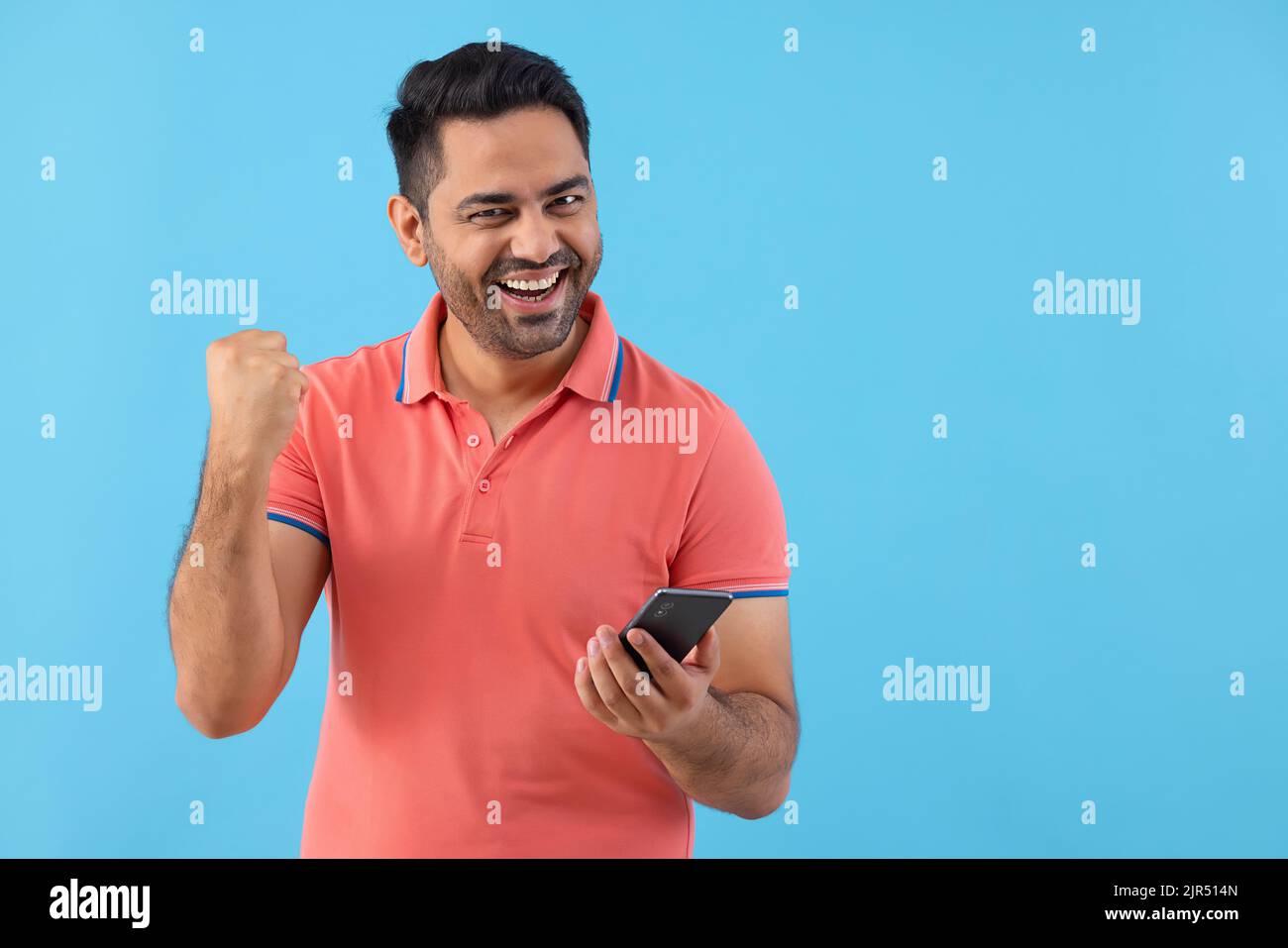 Happy young man cheering with raising his fist while using Smartphone Stock Photo