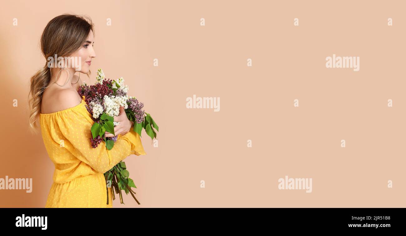 Beautiful young woman holding bouquet of lilac flowers on beige ...
