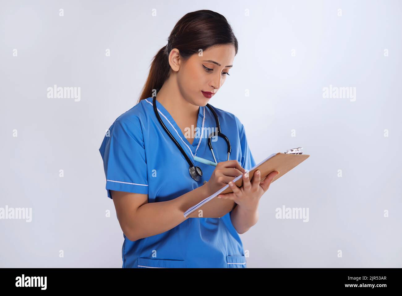 Portrait of a female nurse writing down patient information standing against white background Stock Photo