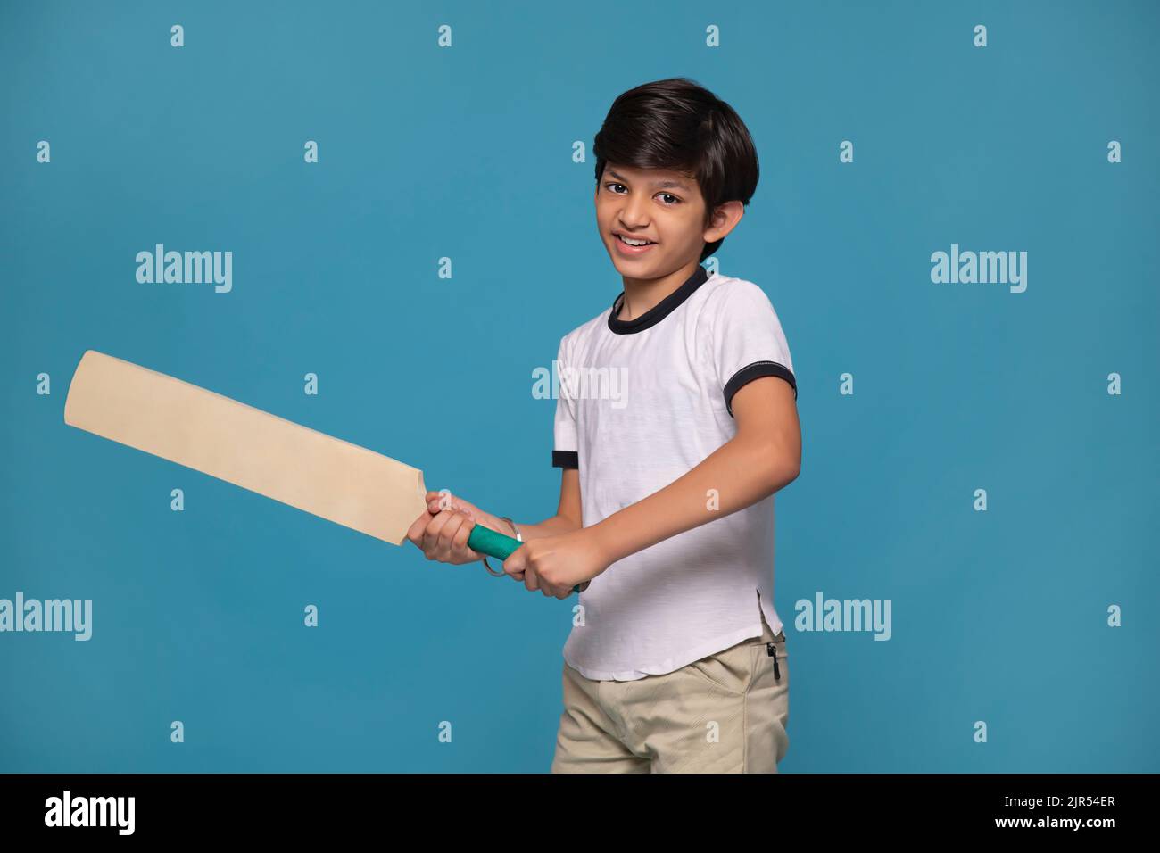 Portrait of a boy batsman ready to face the ball against blue background Stock Photo