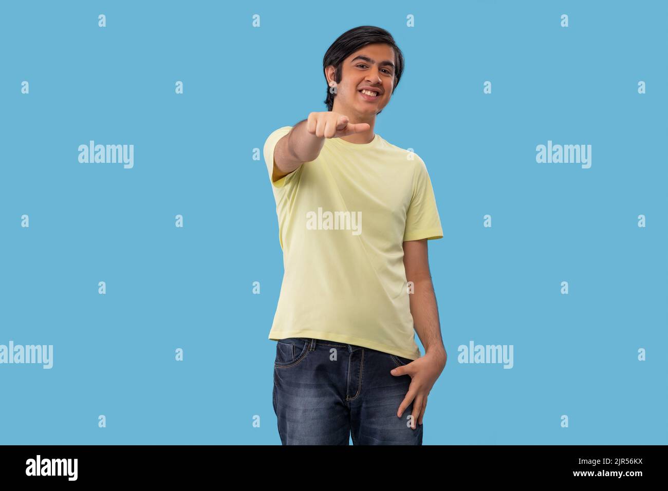 Portrait of a teenage boy pointing towards camera while standing against blue background Stock Photo