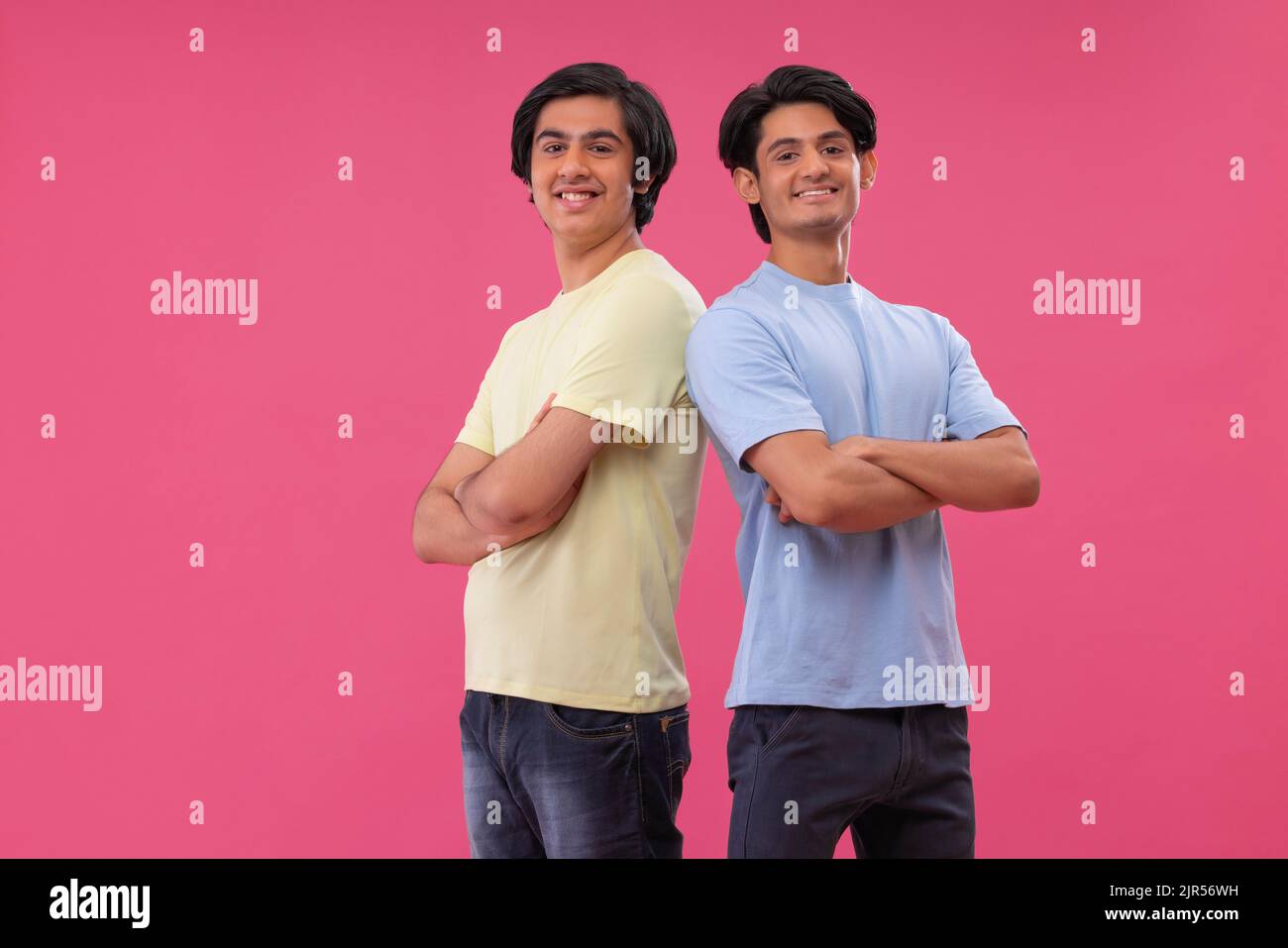 Portrait of two friends standing back to back against pink background ...