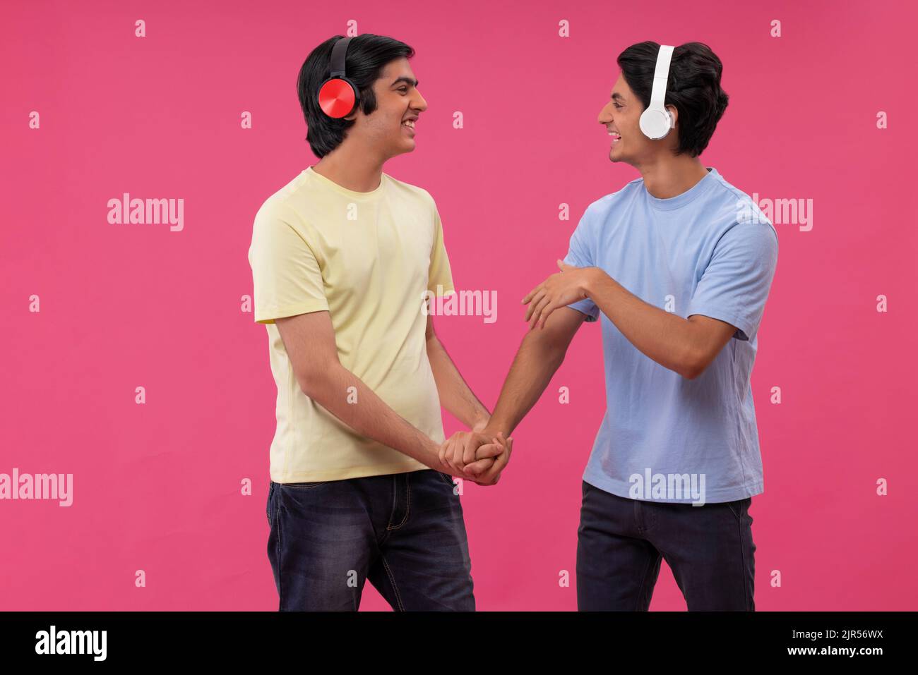 Two happy friends listening to music against pink background Stock Photo