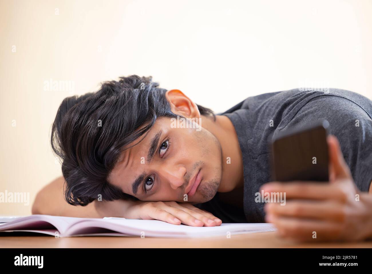 Close-up portrait of a tired teenager leaning head on hand with holding a smartphone Stock Photo