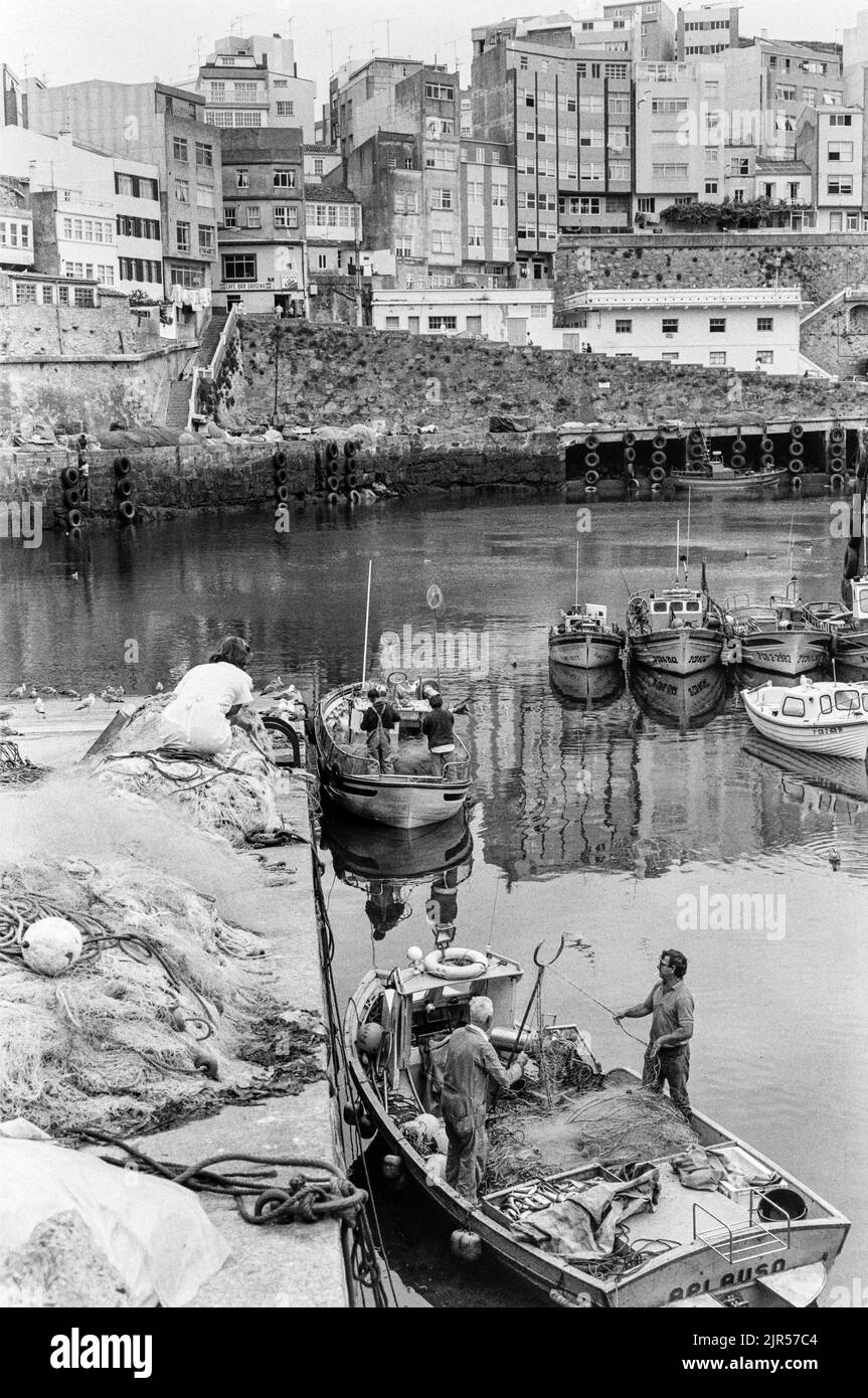 SPAIN - Galicia - 1970s. fishermen preparing their boats in Malpica harbour with the town in the background., Galicia, North west Spain. Copyright Pho Stock Photo