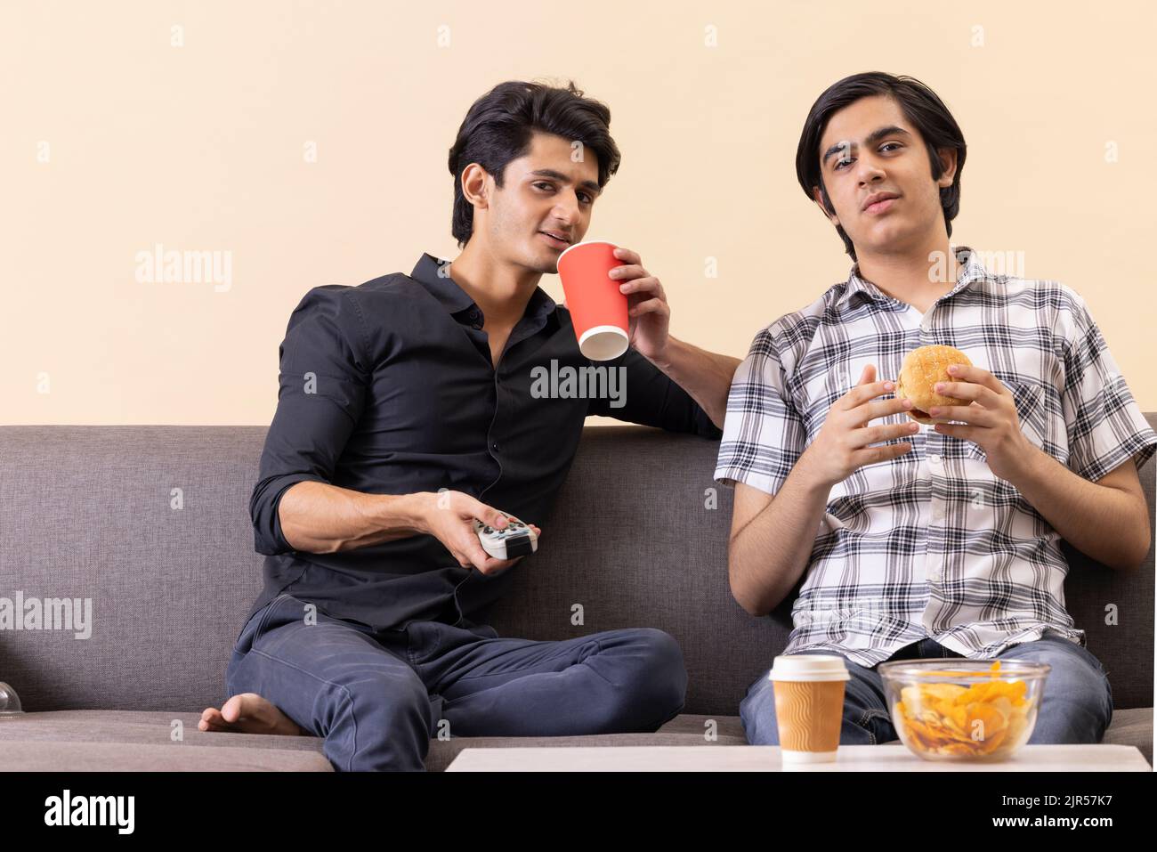 Two happy teenage boys eating fast foods and watching TV together at home Stock Photo