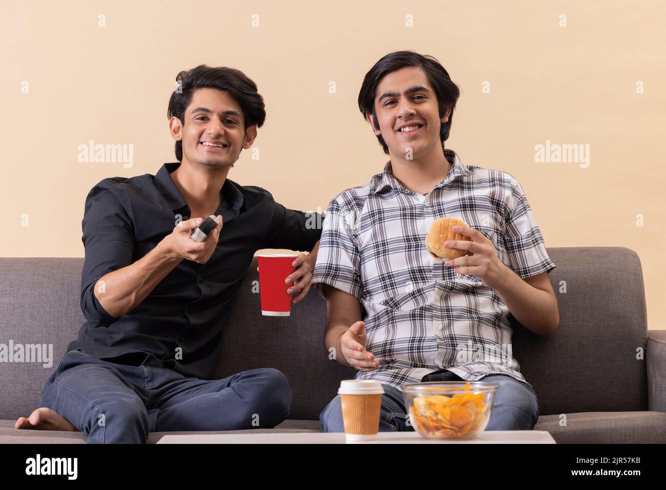 Two happy teenage boys eating fast foods and watching TV together at home Stock Photo