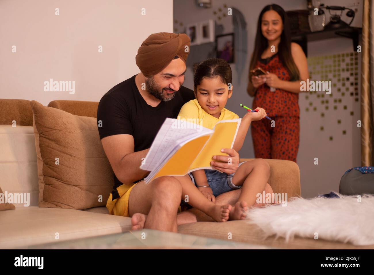 Father helping his daughter with homework while mother standing away Stock Photo