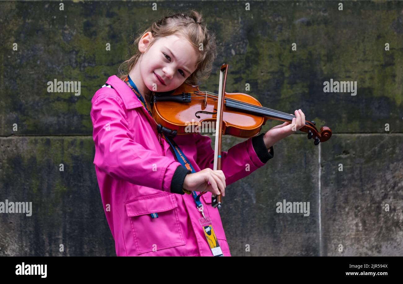 Royal Mile, Edinburgh, Scotland, UK, 22nd August 2022. Fringe performers: a very young street busker called Emma Deimal performs outside St Giles Cathedral playing fiddle music.  Credit: Sally Anderson/Alamy Live News Stock Photo