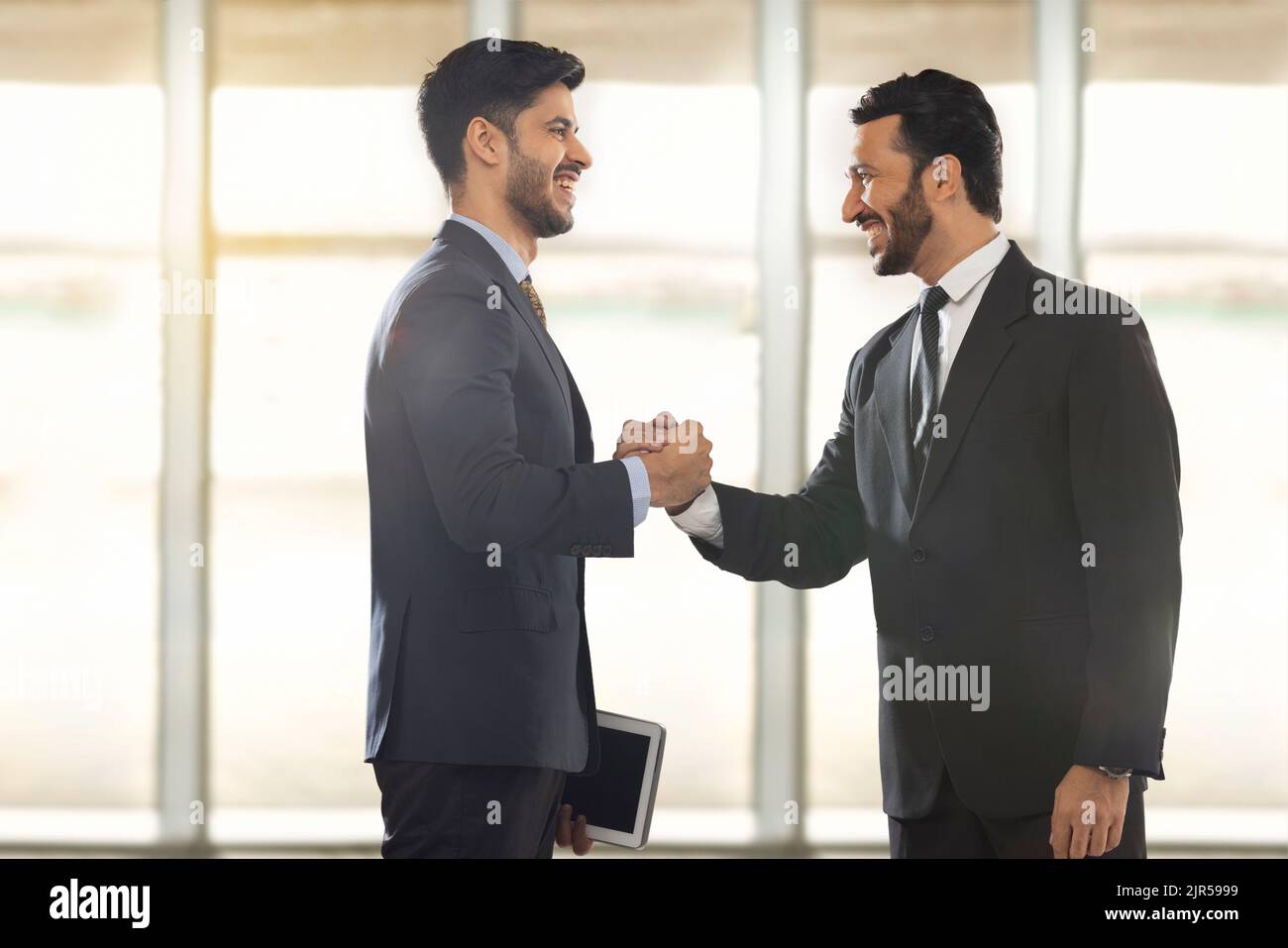 Corporate employees in formal business standing together in office while holding each other's hand with firm grip. Stock Photo