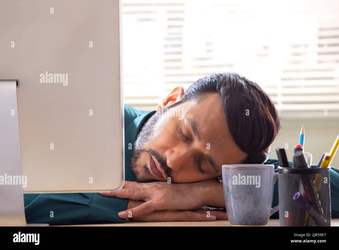 A corporate employee in formal clothing sleeping behind desktop in office. Stock Photo