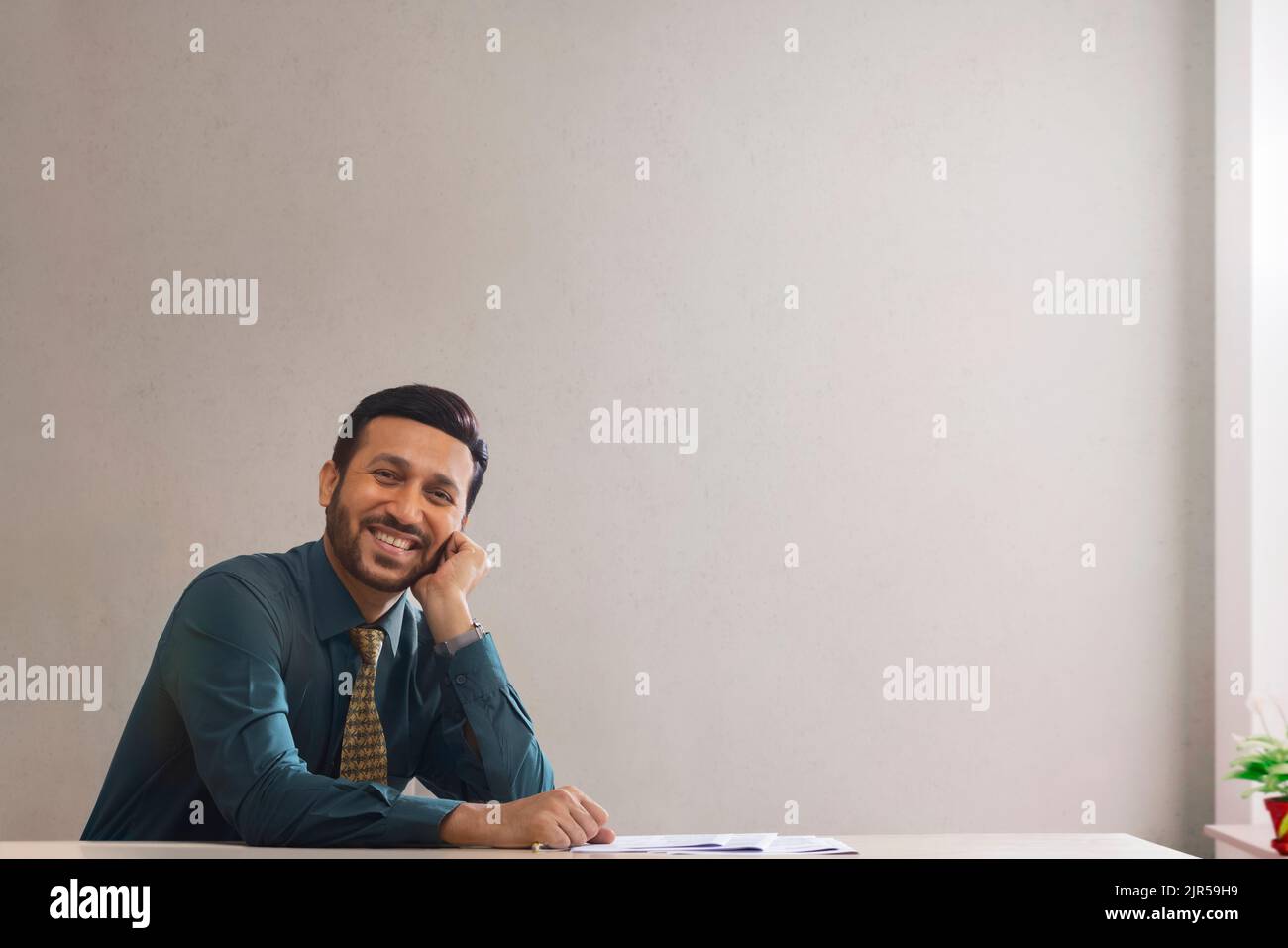 A happy corporate employee in formal clothing sitting with hand on face. Stock Photo