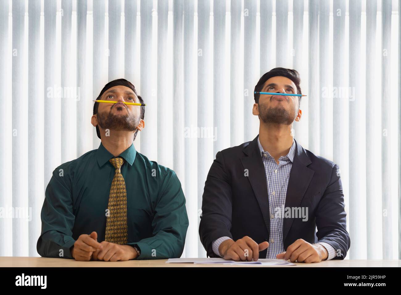 Corporate co-workers sitting together and balancing pencils on their nose. Stock Photo