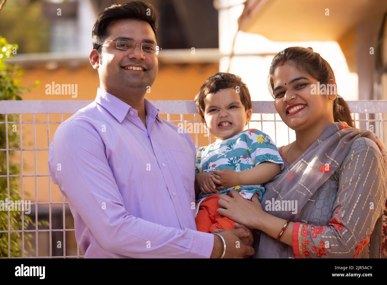 Portrait of happy couple with their child standing in front of gate ...