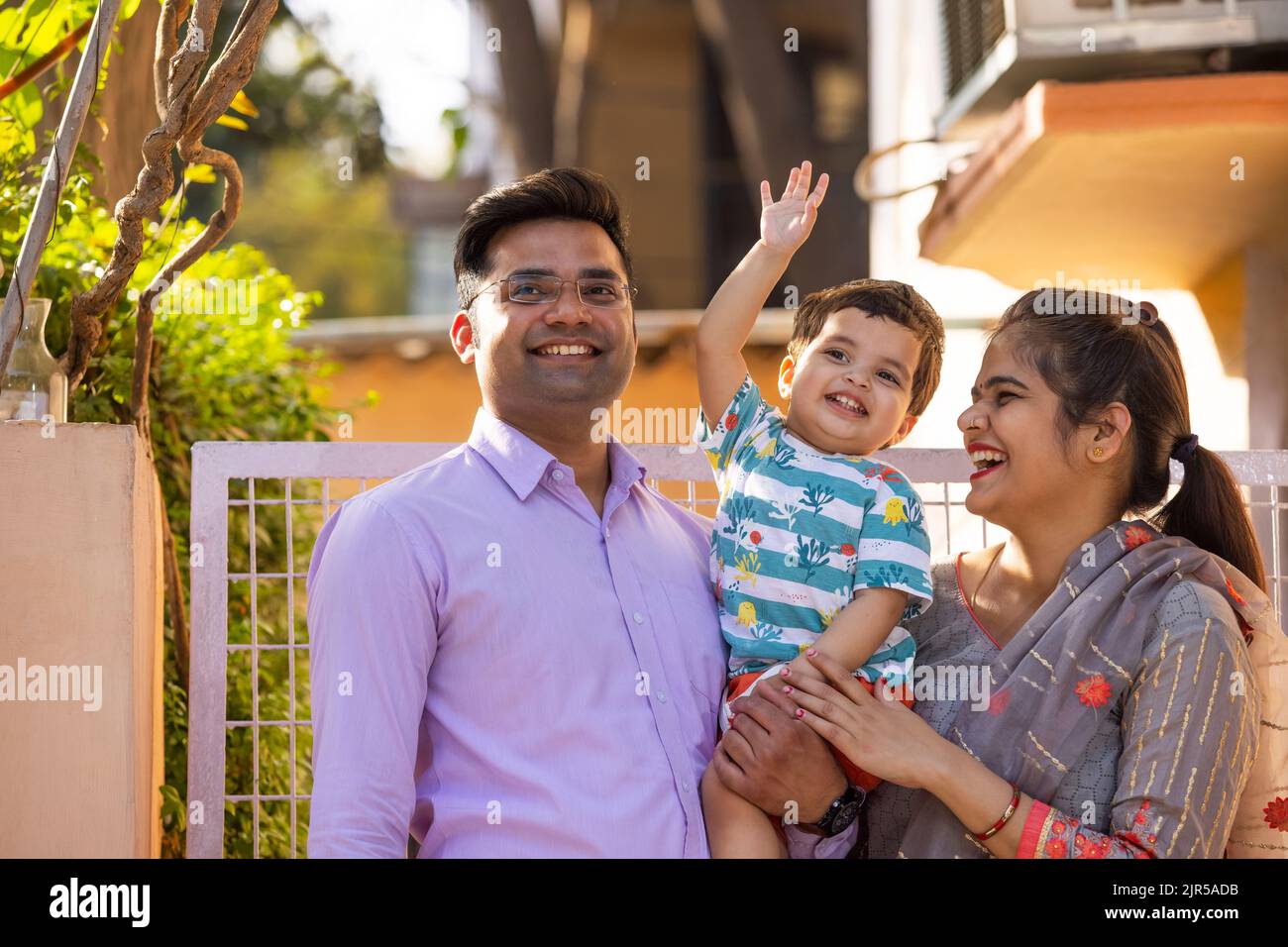 Portrait of happy couple with their child standing in front of gate ...