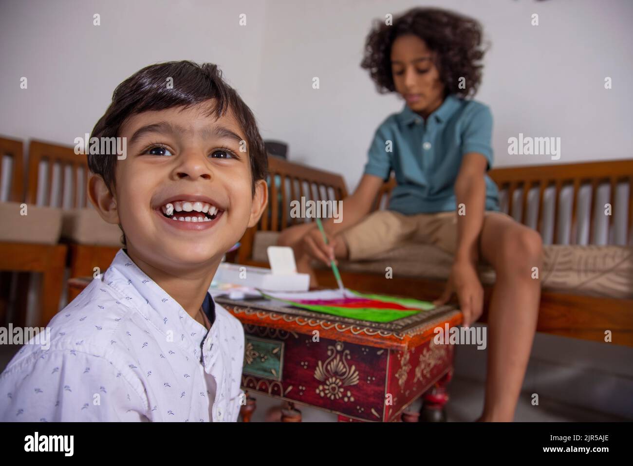 Younger brother smiling and elder brother painting while sitting on sofa Stock Photo