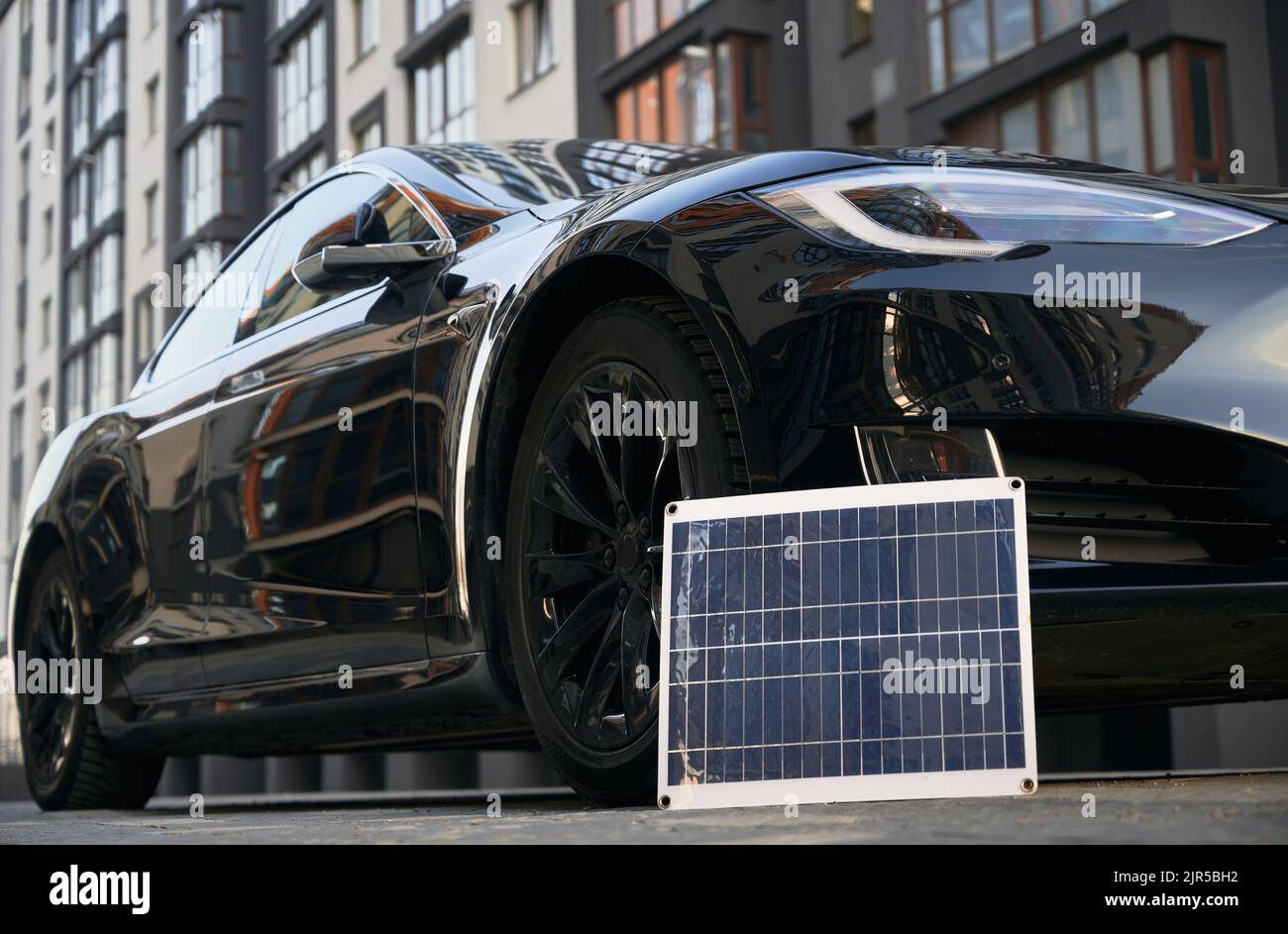 Black electric vehicle and photovoltaic solar panel on city street. Portable solar panel and