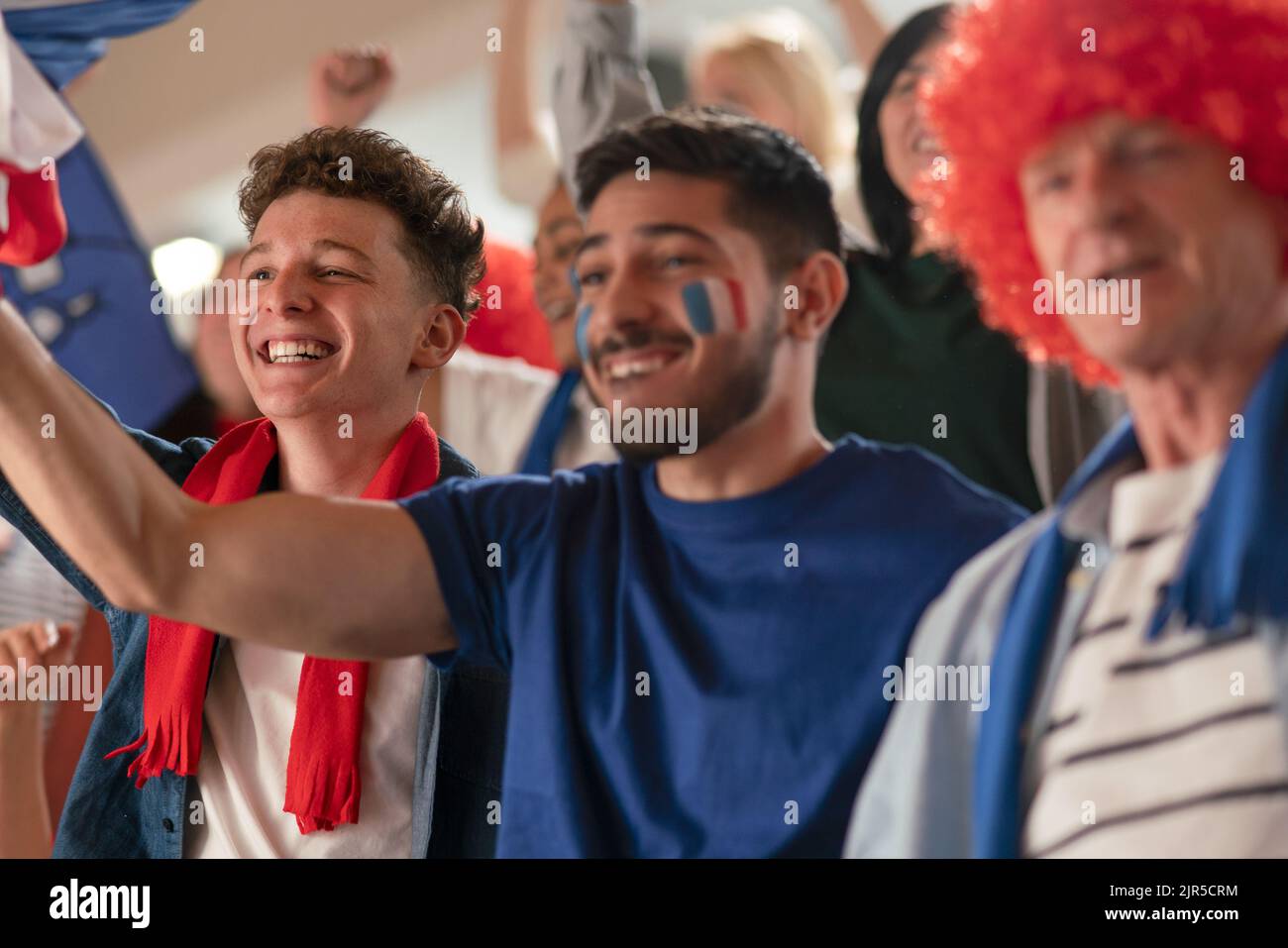 Excited football fans supproting French national team in live soccer match at stadium. Stock Photo