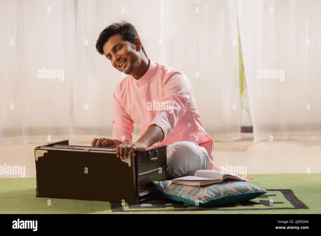 Portrait of young man playing harmonium at home Stock Photo