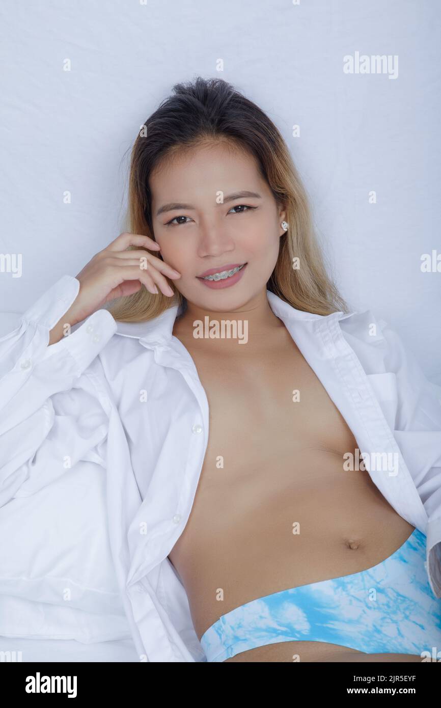 Beautiful Asian woman wearing light Aqua  panties and a men's white shirt on a bed with white sheets Stock Photo