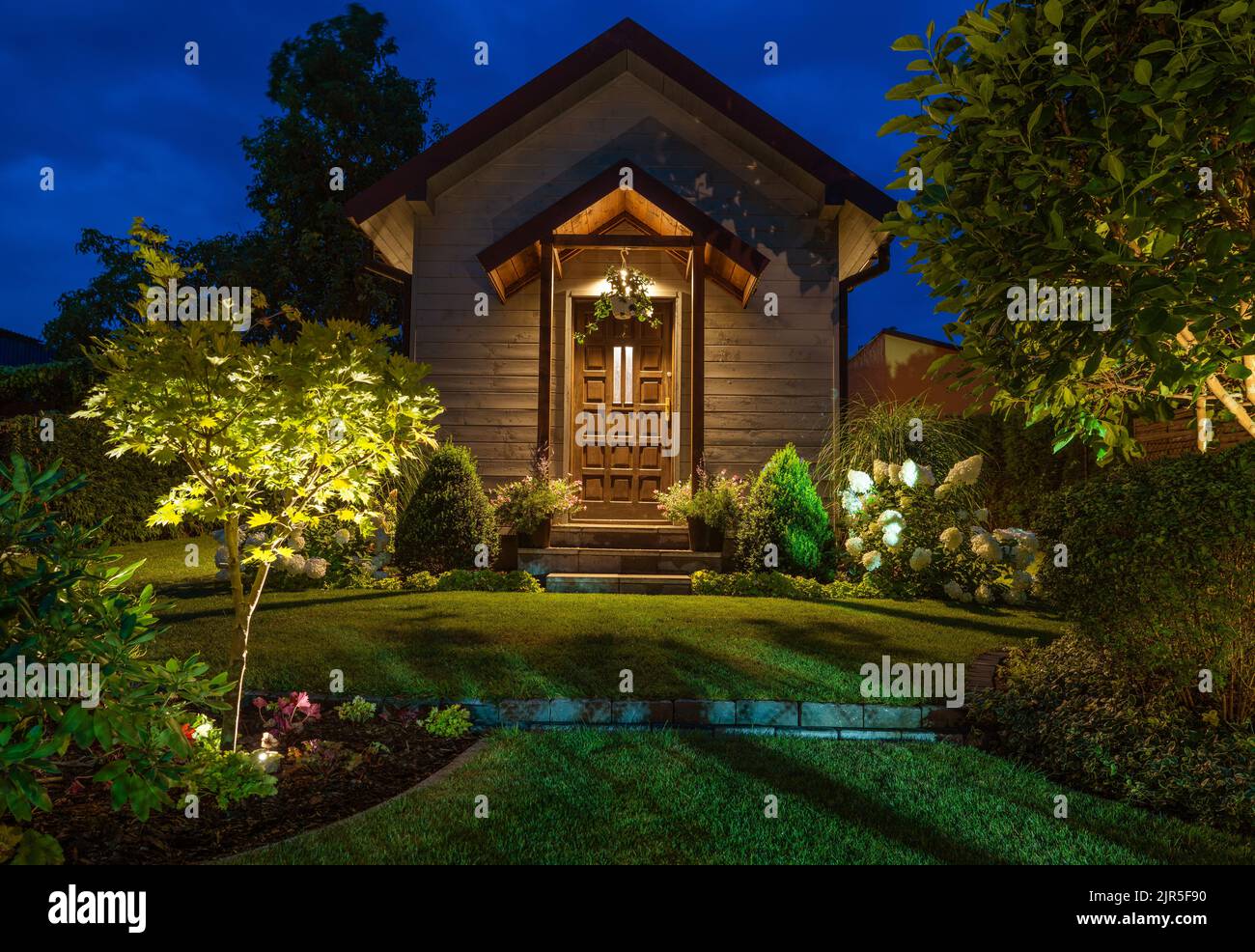 Front of Illuminated Rustic Garden Shed and Beautiful Backyard Garden with LED Lighting