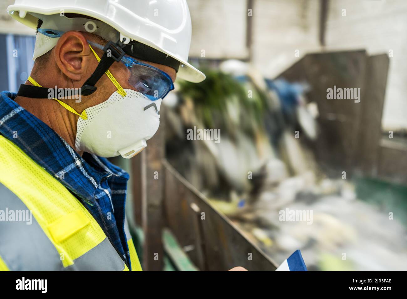 Urban Waste Sorting Facility Technician Making Documentation Staying Next to Trash Moving Conveyor. Stock Photo