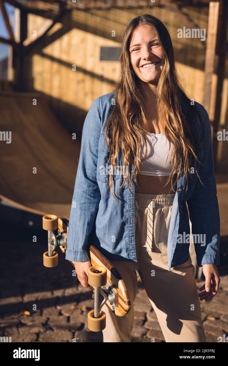 Vertical image of happy caucasian woman holding skateboard in skate shop Stock Photo