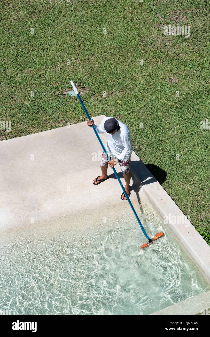 Aerial view of a maintenance worker cleaning a pool with a brush in Mexico, vertical screen Stock Photo