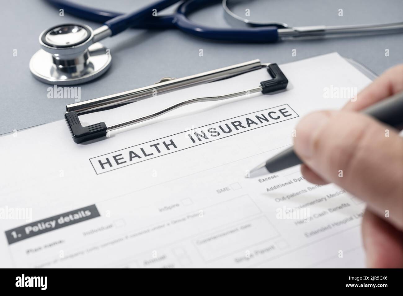 Hand writing on Health Insurance form and stethoscope on desk Stock Photo