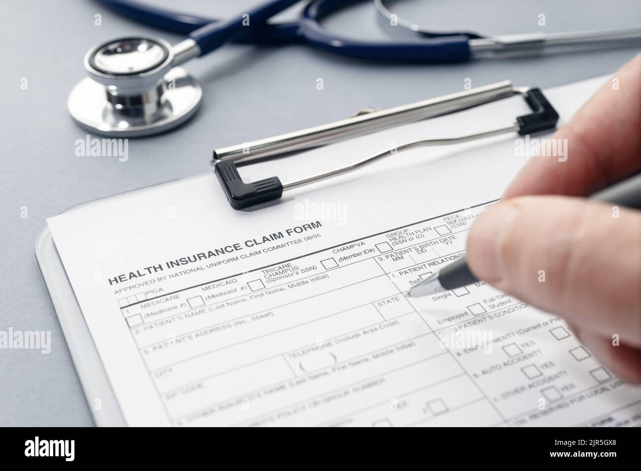 Hand filling on Health Insurance claim form and stethoscope on desk Stock Photo