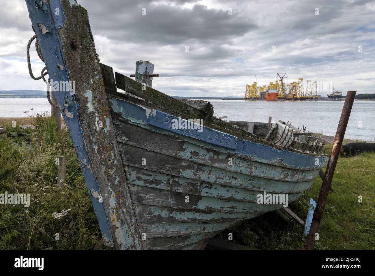 An abandoned boat at Cromarty in the Black Isle. In the distance are bases for offshore wind turbines Stock Photo