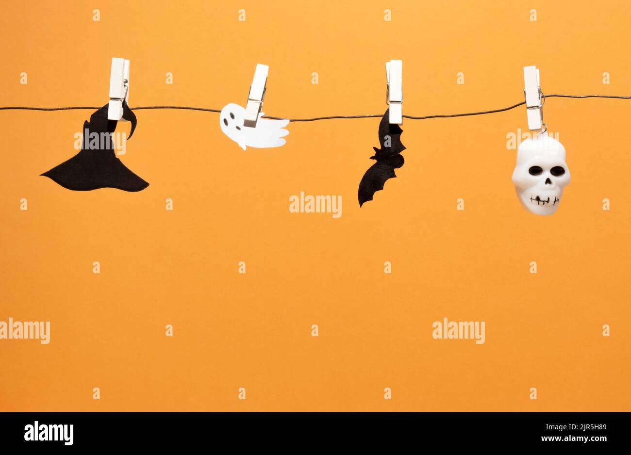 Bat silhouette, skull, ghost and witch's hat on clothesline with clothespins. Orange background with copy space. Trendy Halloween background. Stock Photo