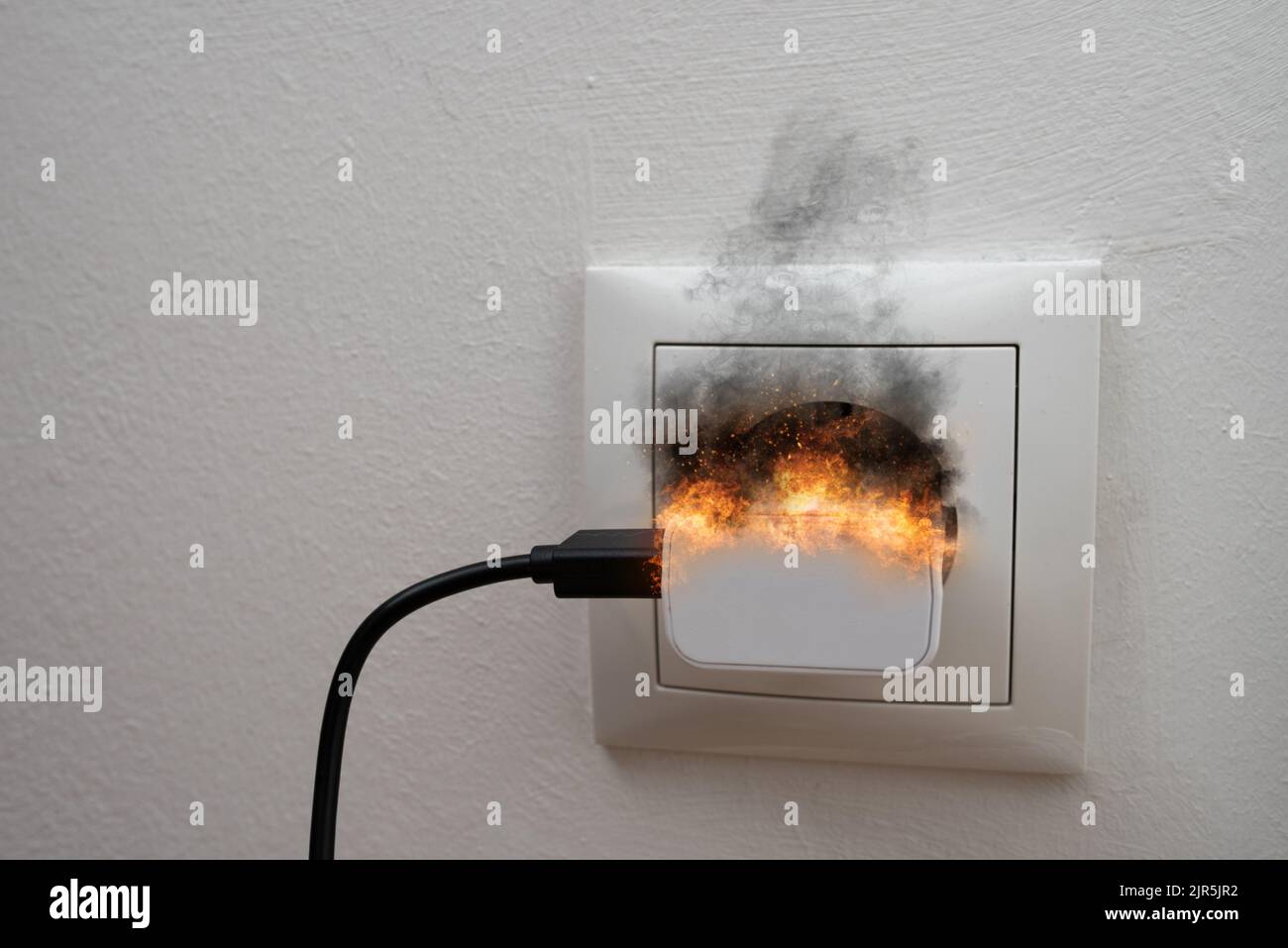 black smoke and sparks coming from charger plugged into wall socket, fire hazard concept Stock Photo