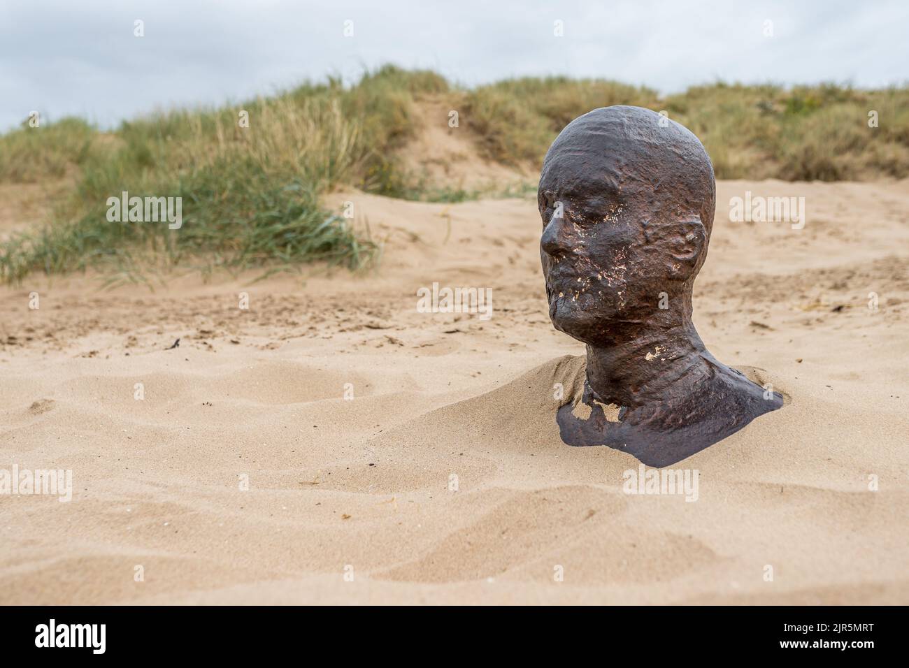 Iron Man up to his neck in sand seen on Crosby beach near Liverpool pictured in August 2022 against sand dunes. Stock Photo