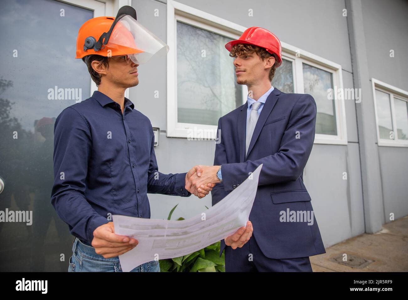 Two engineers shake hands while looking at a floor plan during construction Stock Photo