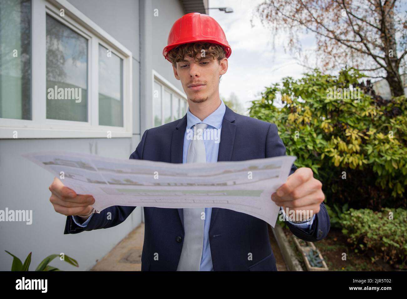 an engineer analyzes a floor plan while he is wearing a protective helmet Stock Photo