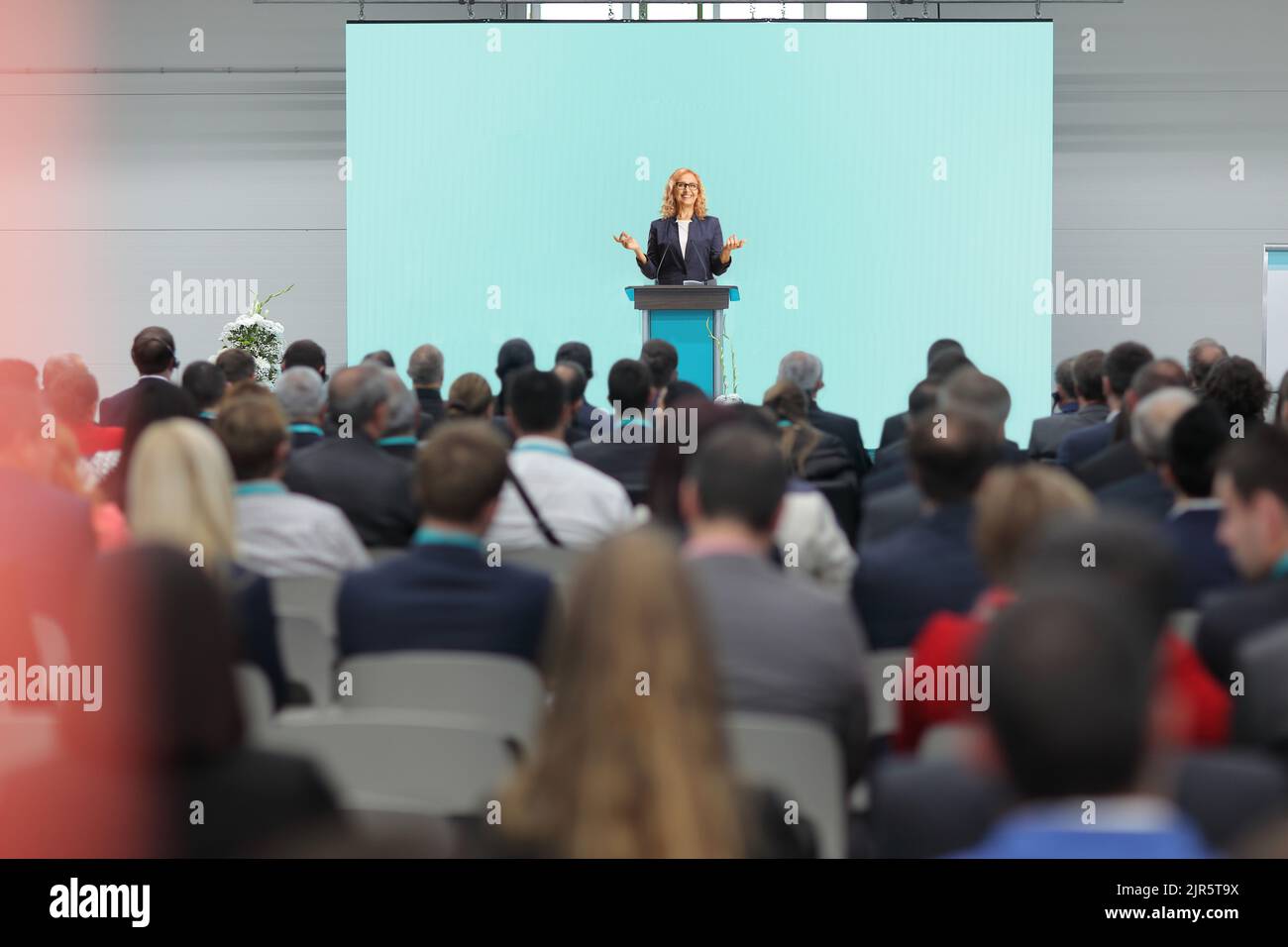 Woman giving a speech on a podium and people sitting in the audience at a business conference Stock Photo