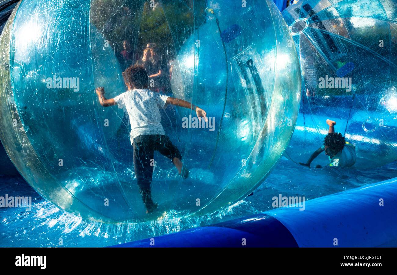 Two boys struggle to stay upright as they play inside  floating water balls on Eastbourne seafront in East Sussex, UK. Stock Photo