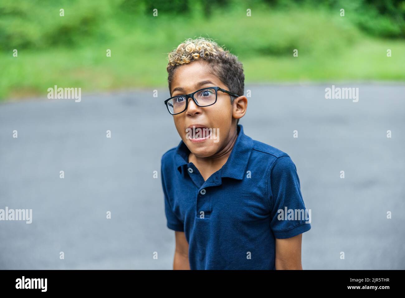 An African American elementary aged boy wearing glasses standing make a shocked scared silly face Stock Photo