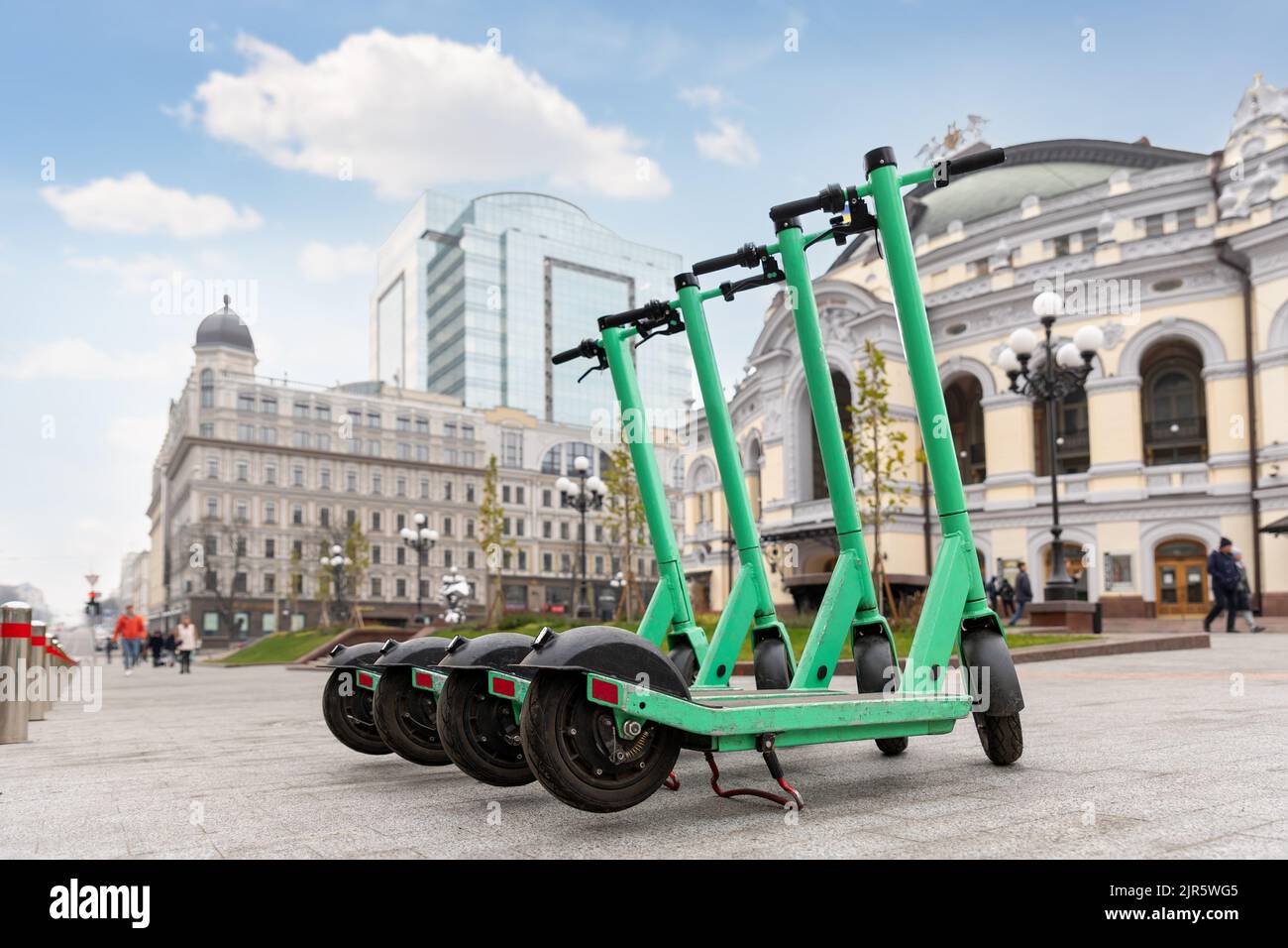 Many modern green electric scooters sharing parked city street. Self