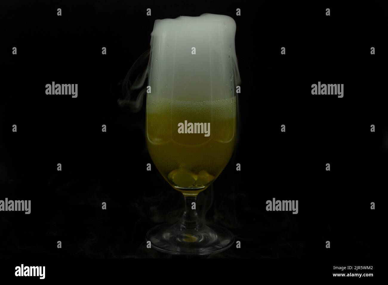 Beer glass containing fresh liquid with cooling dry ice cooling emanates white smoke outlining the profile of the glass in celebration of Halloween pa Stock Photo
