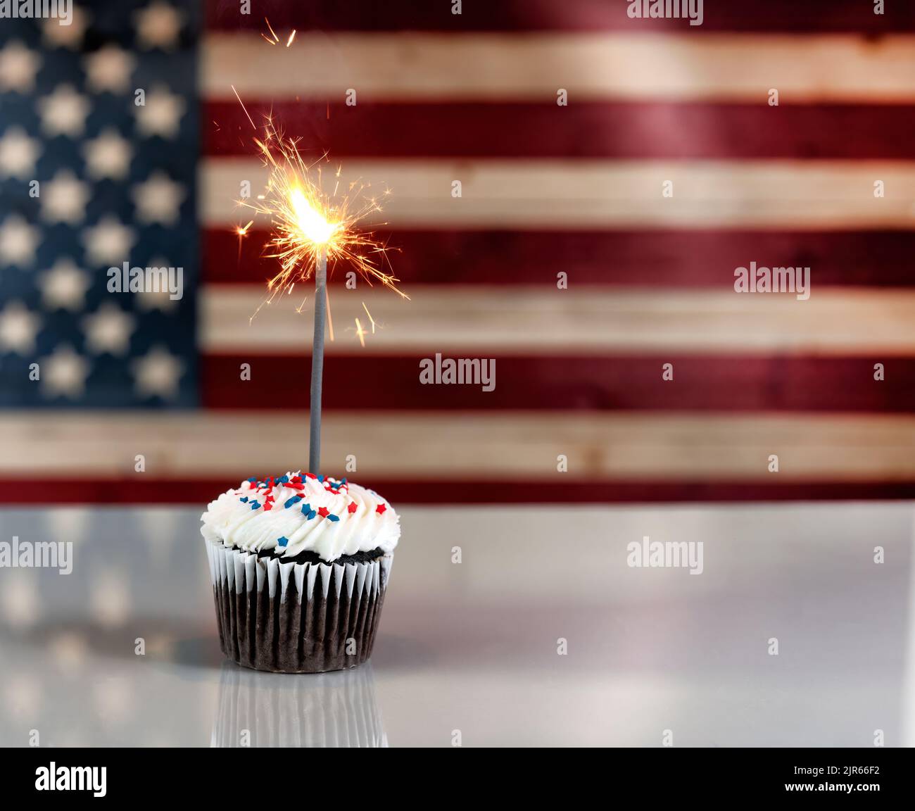 USA Independence Day celebration with decorated cupcake and glowing sparklers with flag in background Stock Photo